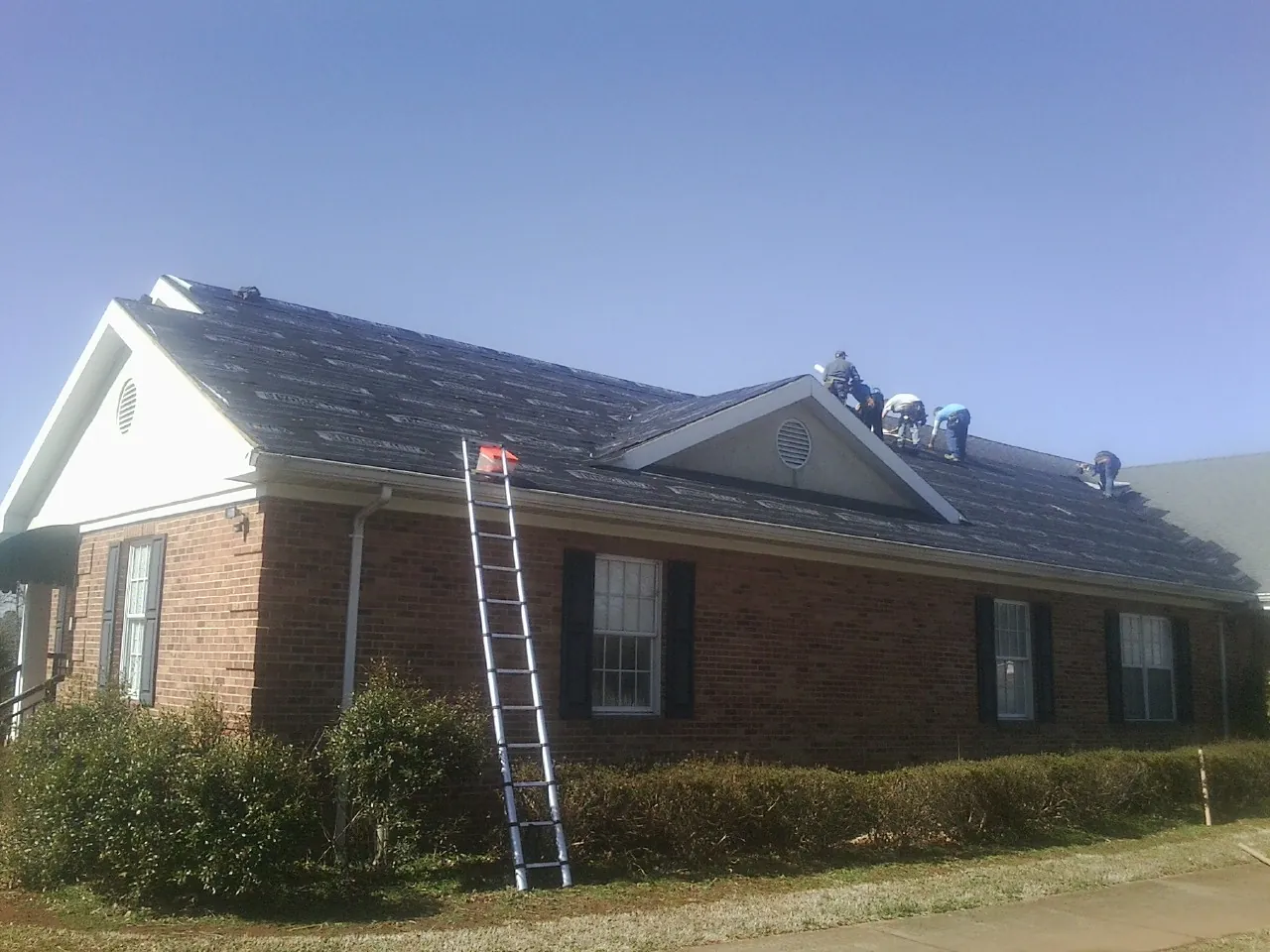 Crew tearing shingles off a brick ranch roof with a ladder set — Emergency Roof Repair work by our crew in Gaylordsville