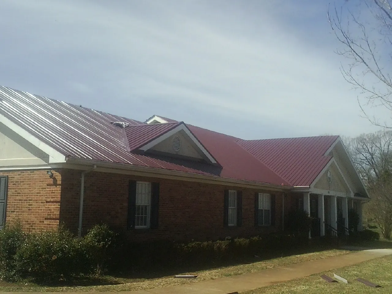 Red metal roof with gabled entries on a long brick building, from a Hail Damage Roof Repair job in Gaylordsville