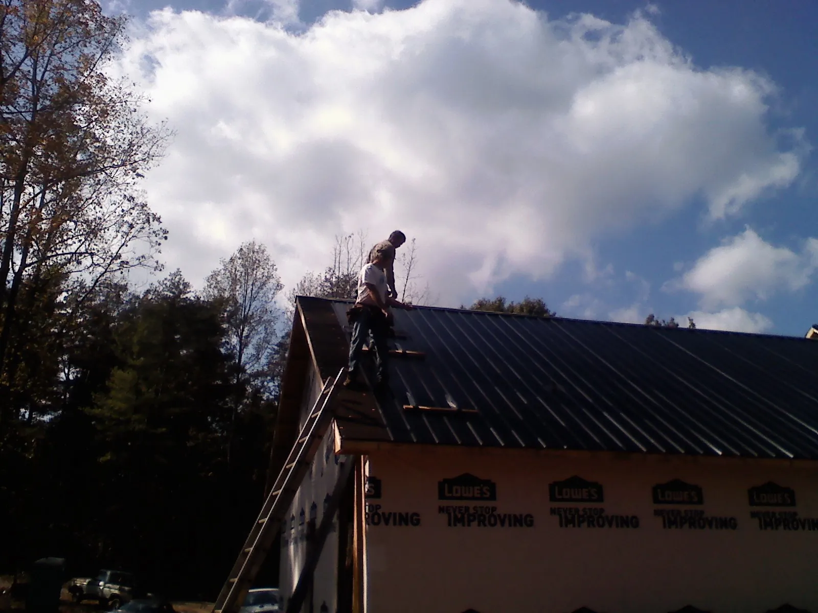 Roofer fastening dark metal panels high against a cloudy sky, from a Roof Inspection job in Gaylordsville