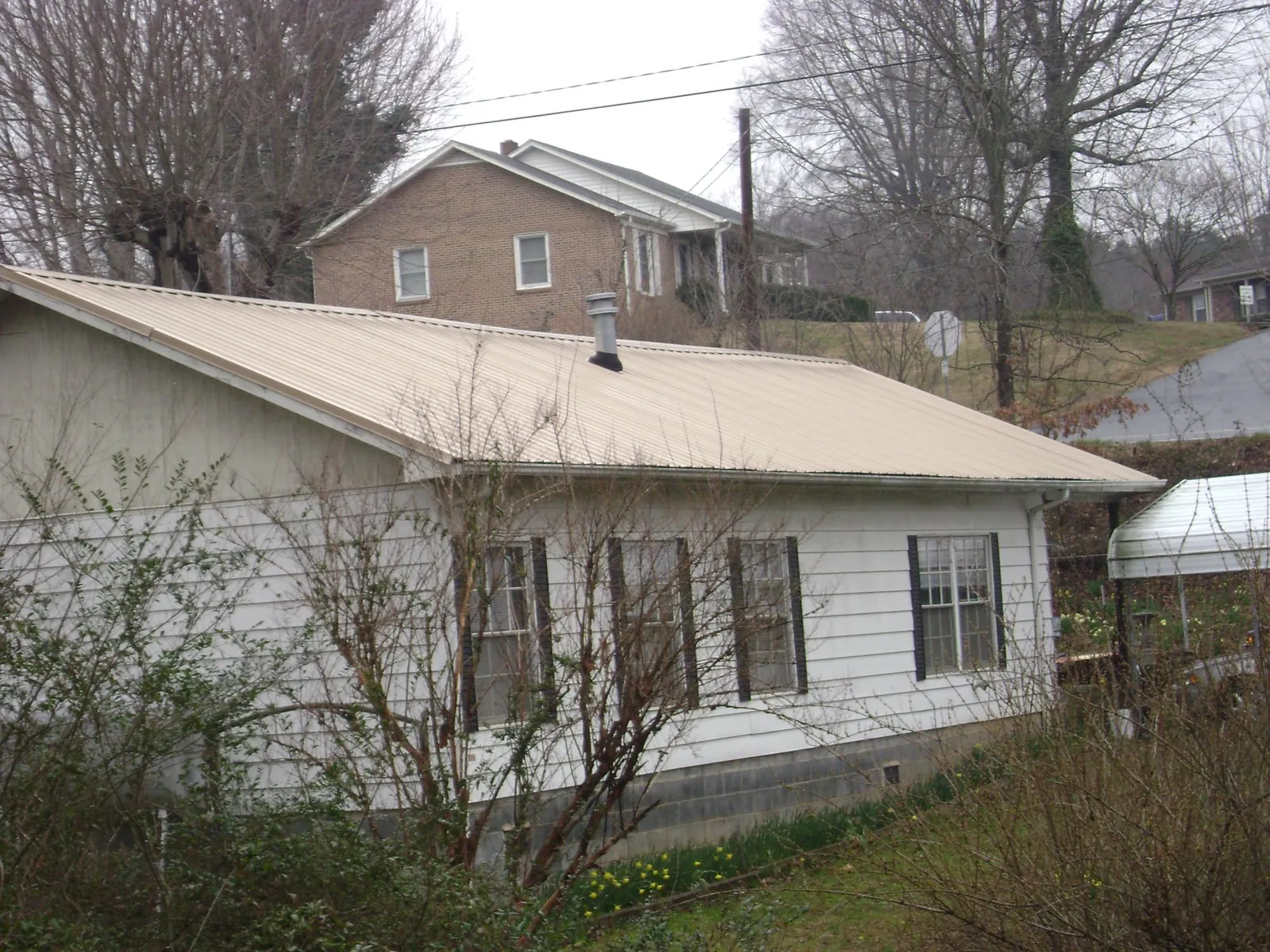 Tan metal roof on a white sided house set into a hillside — Commercial Roofing by Roofing Brothers in Gaylordsville